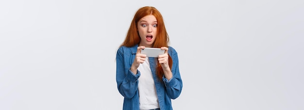 Verbaasde geschrokken schattige roodharige vrouw heeft zojuist de uitdaging gewonnen in een geweldig spel met de horizon van de smartphone