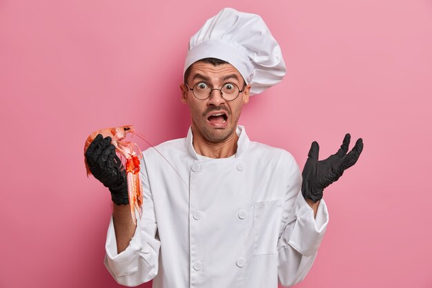 Verbaasde professionele verraste chef-kok houdt visproducten vast, bereidt een heerlijk gastronomisch gerecht, roept negatief uit