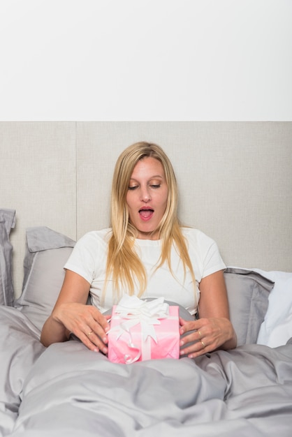 Verbaasde vrouw in bed met geschenkdoos