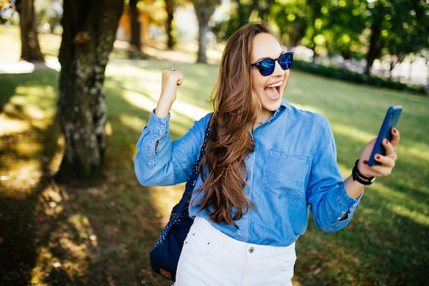 Verbaasde vrouw, met overwinningsschreeuw, kijk naar de telefoon, krijg goed nieuws buiten in een park