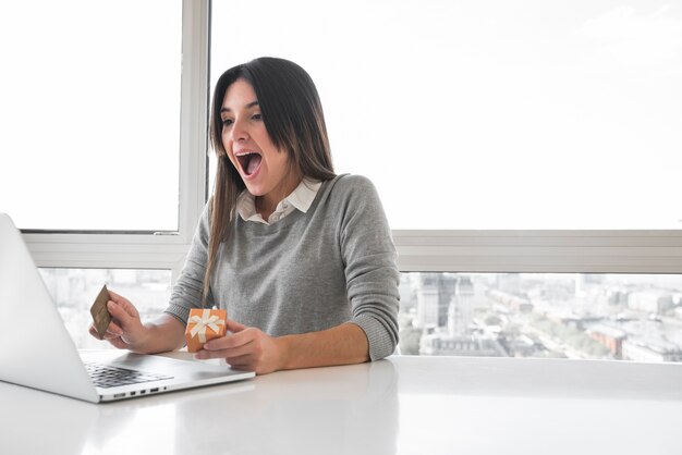 Verbaasde vrouwenzitting bij lijst met laptop