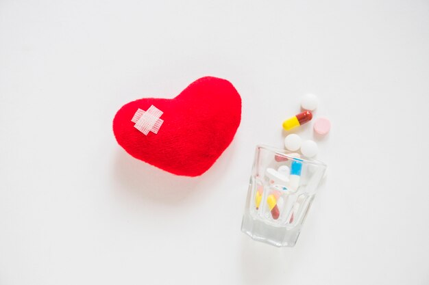 Verband op rood hart dat met vele pillen wordt gevuld die van glas op witte achtergrond morsen