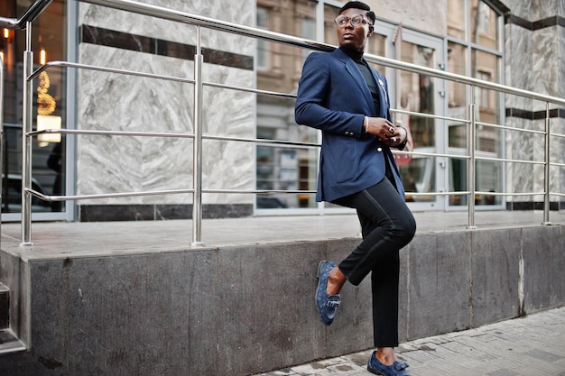 Verbazingwekkend uitziende Afro-Amerikaanse man draagt blauwe blazer met broche zwarte coltrui en bril op straat Modieuze zwarte man
