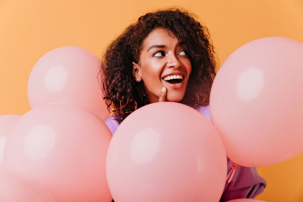 Verbazingwekkend zwart vrouwelijk model met partijballons die zich voordeed op oranje. schattige brunette vrouw plezier tijdens evenement.