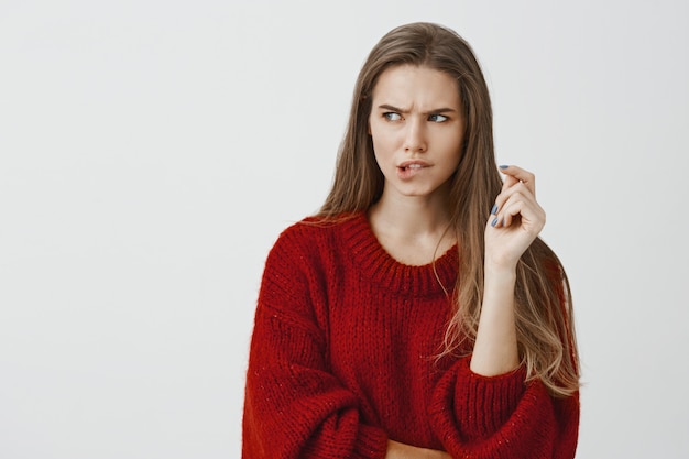 Verdachte vriendin probeert een manier te bedenken om het wachtwoord van de smartphone te kiezen. Portret van gefocuste angstige goed uitziende vrouw, lip bijten en fronsen, opzij kijken, denken oplossing voor probleem