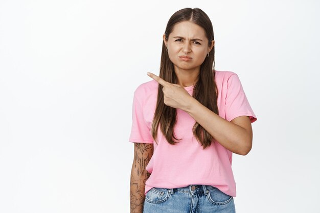 Verdrietig en sombere jonge vrouw die met de vinger naar links wijst en een teleurgestelde witte achtergrond fronst