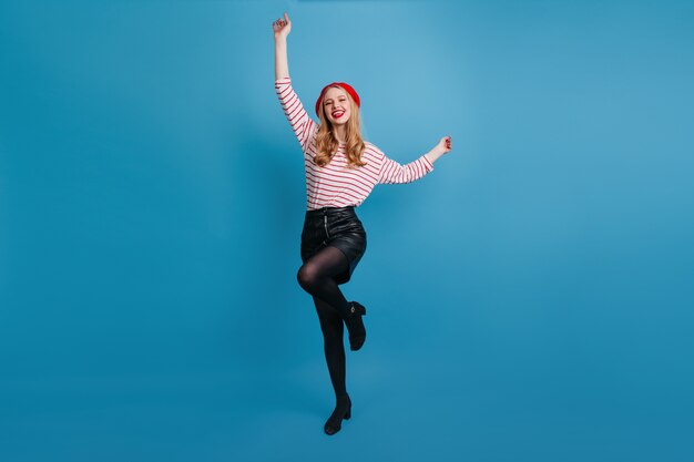 Verfijnd blondemeisje die en handen dansen zwaaien. prachtige Franse vrouw poseren op blauwe muur.