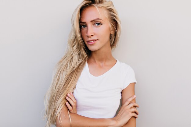 Verfijnde Europese vrouw poseren met gekruiste armen. Enthousiaste jongedame met blond haar die geniet van fotoshoot.