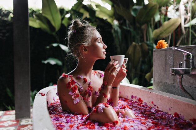 Verfijnde vrouwenzitting in bad op aardachtergrond. Prachtige blanke dame ontspannen tijdens spa en het drinken van thee.