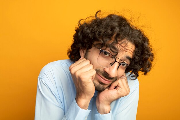 Vergrote weergave van de jonge knappe blanke man met bril kijken camera geïsoleerd op een oranje achtergrond 87