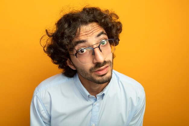 Vergrote weergave van de jonge knappe man met bril kijken voorzijde geïsoleerd op oranje muur