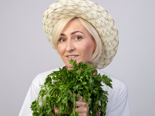 Vergrote weergave van een glimlachende blonde tuinmanvrouw van middelbare leeftijd in uniform met een hoed met twee trossen koriander