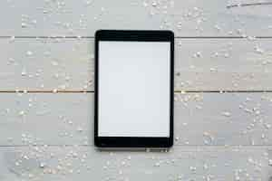 Gratis foto verhoogde mening van digitale tablet met verspreide haver op houten plank