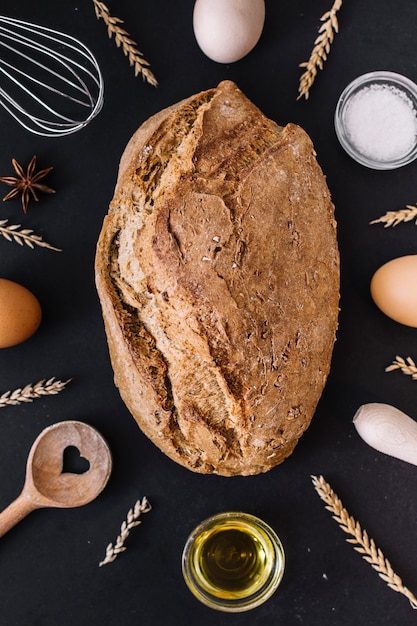 Verhoogde mening van heerlijk brood met diverse bakselingrediënten en werktuigen op zwarte oppervlakte