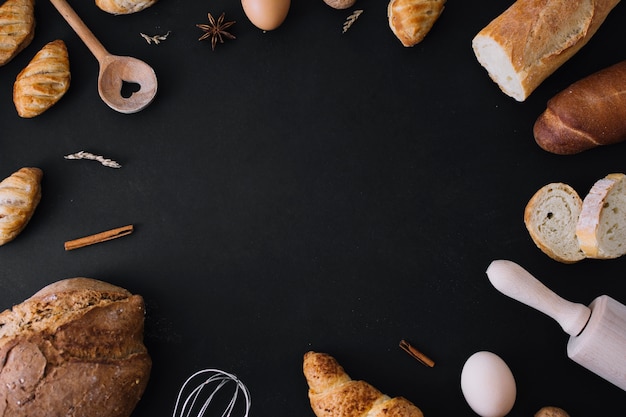Verhoogde weergave van brood; keukengerei; ei en kruiden vormen frame op zwarte achtergrond