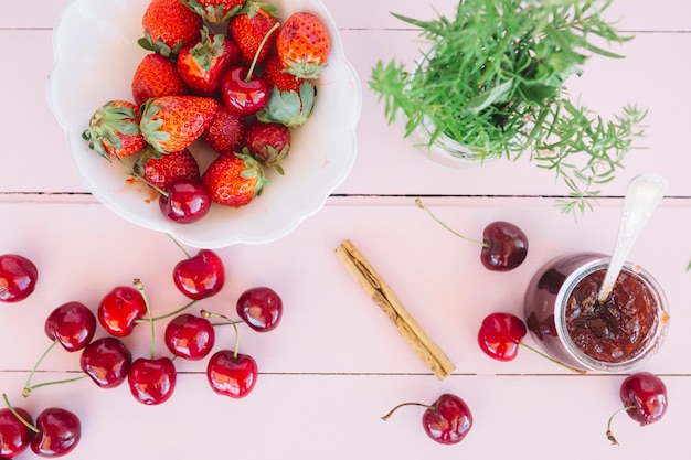 Gratis foto verhoogde weergave van jam; kersen en rozemarijn in de buurt van verse aardbeien in kom