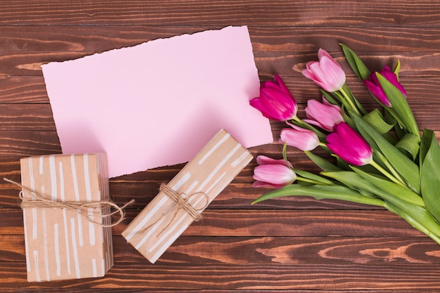 Verhoogde weergave van roze tulp bloemen; roze papier; en geschenkdozen tegen houten oppervlak