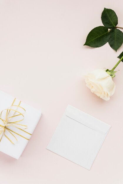 Verhoogde weergave van witte bloem; geschenk en envelop op gekleurde achtergrond