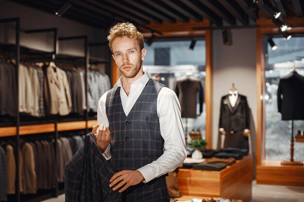 Verkoop, winkelen, mode, stijl en mensen concept. Elegante jongeman die kleding kiest in winkelcentrum of kledingwinkel.