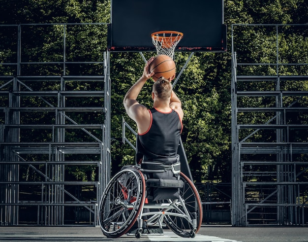 Verlamde basketbalspeler in rolstoel speelt basketbal op openluchtgrond.