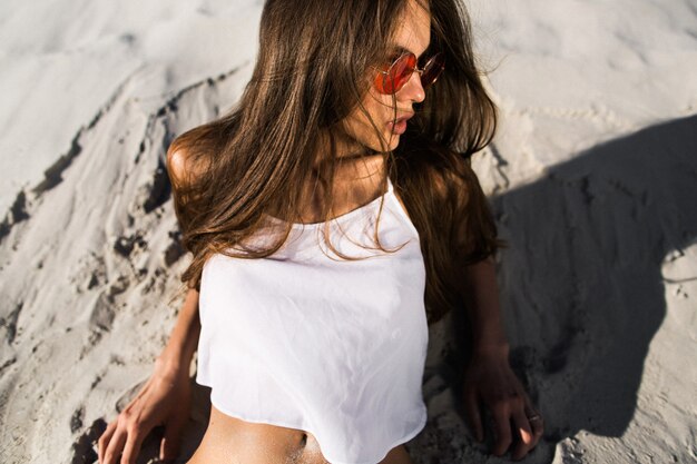 Verleidelijke jonge vrouw in rode zonnebril ligt op wit zand