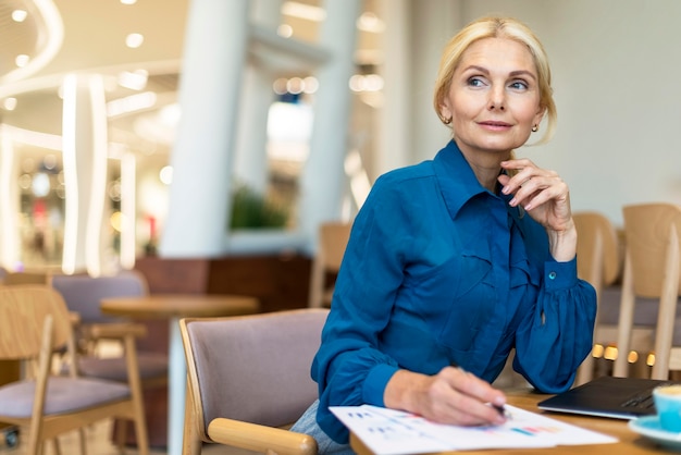 Verleidelijke oudere zakenvrouw omgaan met wat papier tijdens het werken op laptop