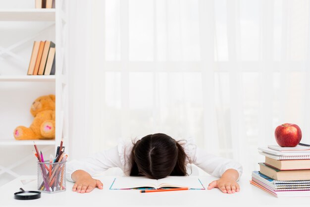 Vermoeid schoolmeisje dat over voorbeeldenboek ligt