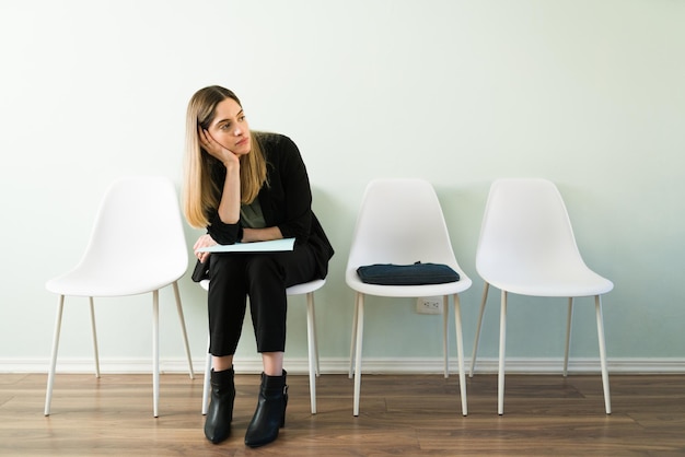 Vermoeide blanke vrouw in een professioneel pak voelt zich verdrietig tijdens het wachten op de benoeming van haar sollicitatiegesprek bij een wervingsbureau