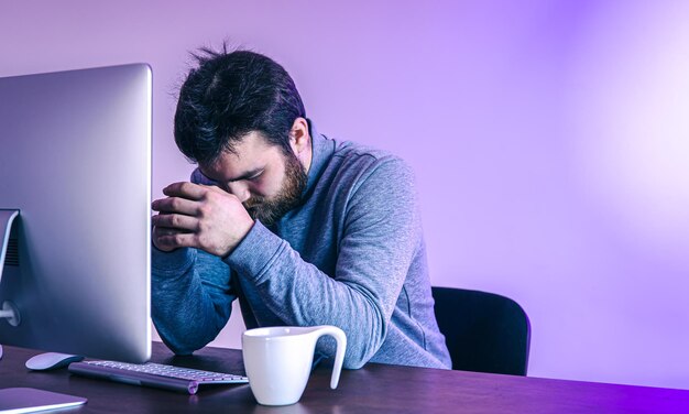 Vermoeide man zit voor een computer met een kopje koffie gekleurde verlichting