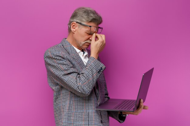 Vermoeide oude man die laptop vasthoudt terwijl hij op de violette muur blijft?