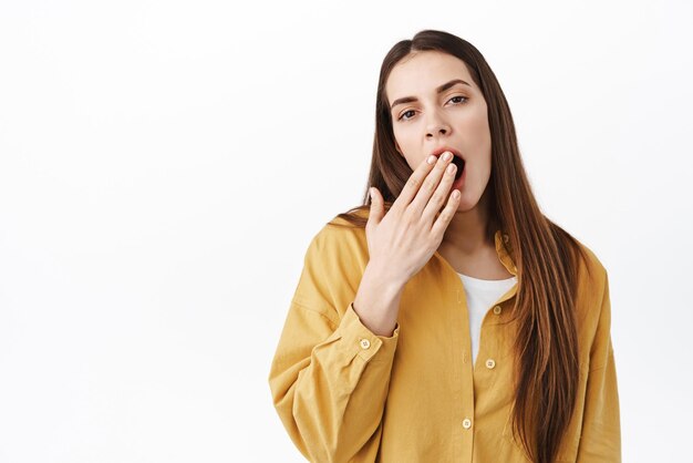 Vermoeide volwassen vrouw geeuwen die betrekking hebben op geopende mond met de hand en slaperig kijken uitgeput zijn wil slapen staande tegen een witte achtergrond Kopieer ruimte