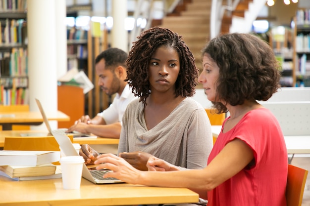 Vermoeide vrouwen die laptop met behulp van bij bibliotheek