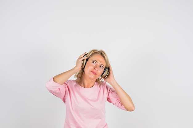 Verouderde peinzende vrouw in roze blouse met hoofdtelefoons