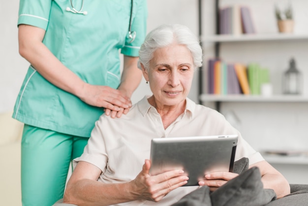 Verpleegster die zich dichtbij hogere vrouw bevindt die digitale tablet gebruikt