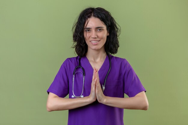 verpleegster draagt uniform en stethoscoop hand in hand in gebed namaste gebaar dankbaar en gelukkig voelen op geïsoleerde groen