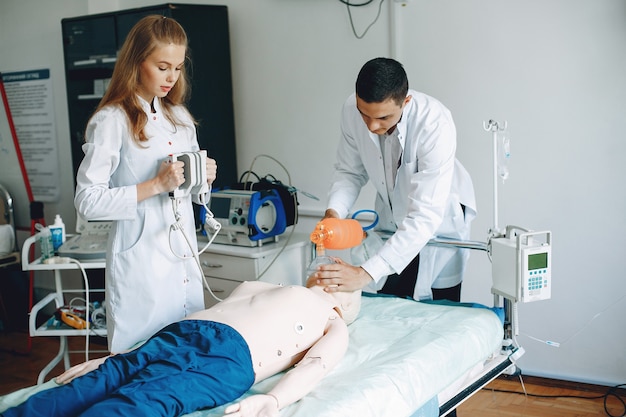 Verpleegster voert reanimatie uit. Dokter helpt vrouw om de operatie uit te voeren. Studenten oefenen geneeskunde uit.