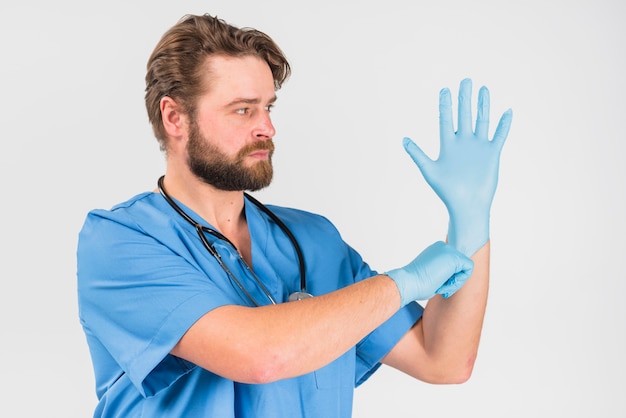 Verpleegstersmannetje met ernstig gezicht dat op handschoenen trekt