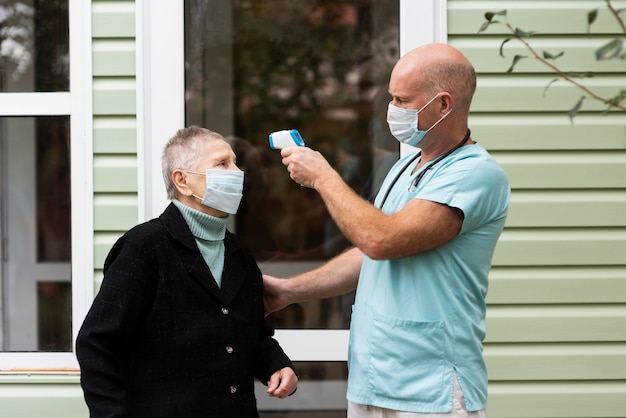 Gratis foto verpleger die een thermometer gebruikt om de temperatuur van de oudere vrouw te controleren