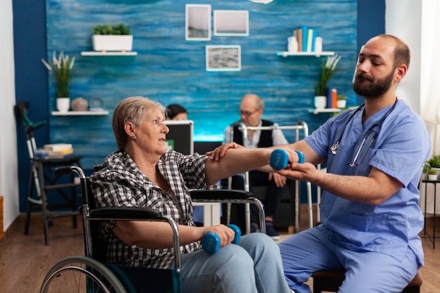 Gratis foto verpleger helpt senior gepensioneerde gehandicapte vrouw in rolstoel te revalideren met dumbbels