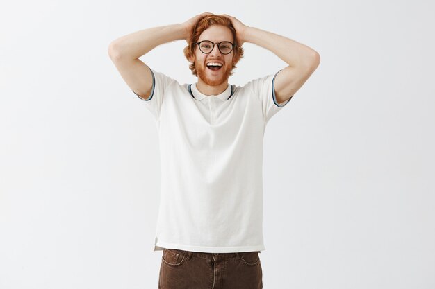 Verrast bebaarde roodharige man poseren tegen de witte muur met bril