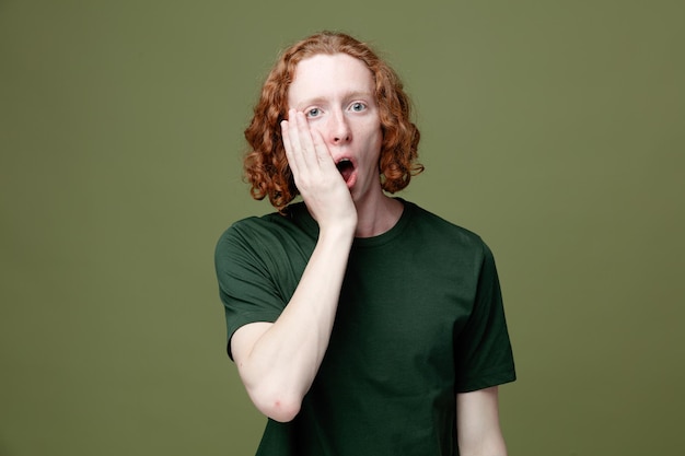 Gratis foto verrast bedekte mond met hand jonge knappe kerel met groen t-shirt geïsoleerd op groene achtergrond