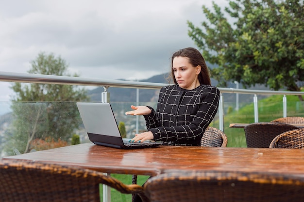 Verrast bloggermeisje toont handgebaar op laptopscherm op de achtergrond van de natuurweergave
