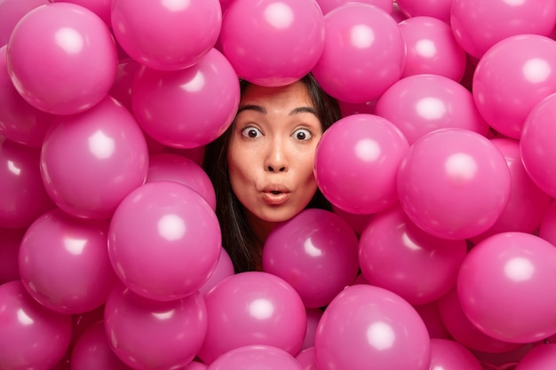 Verrast brunette feestvarken staart met uitgestoken ogen houdt hoofd door opgeblazen ballonnen balloon