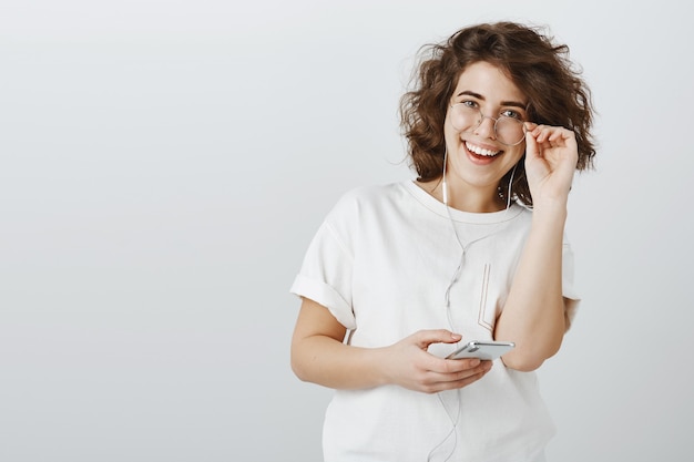 Verrast en geïnteresseerde jonge vrouw die opgewonden kijkt tijdens het gebruik van oortelefoons en mobiele telefoon