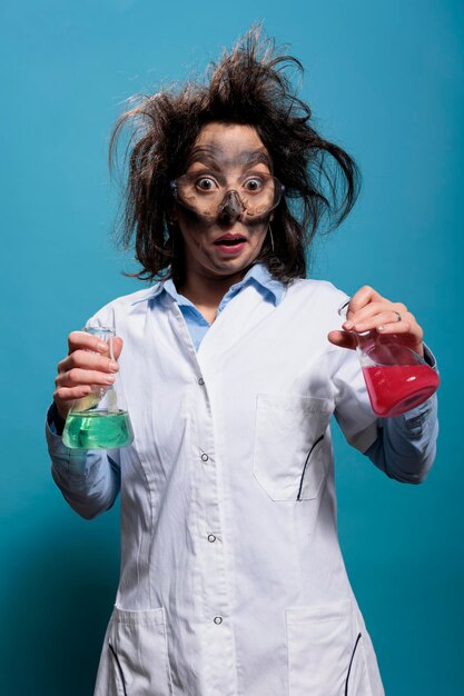Verrast gekke chemiespecialist met glazen bekers gevuld met gevaarlijke vloeibare verbindingen. Gekke scheikundige met vies gezicht en rommelig haar met kolven gevuld met onbekende chemische stoffen.