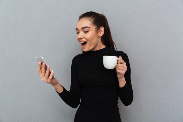 Verrast gelukkig brunette vrouw in zwarte kleding kijken naar smartphone