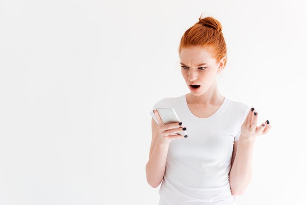 Verrast gember vrouw in t-shirt op zoek naar haar smartphone