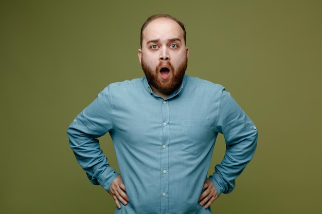 Gratis foto verrast handen op de heupen jonge knappe kerel met blauw shirt geïsoleerd op groene achtergrond