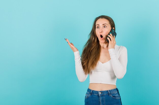 Verrast jong meisje praat op mobiel op blauwe achtergrond