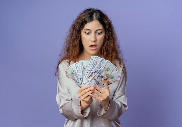 Verrast jong mooi meisje houden en kijken naar contant geld geïsoleerd op blauw